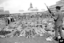 FILE - Police stand guard over Thai student protesters lying on a soccer field at Thammasat University, in Bangkok, Thailand, Oct. 6, 1976.