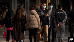 People wearing face masks to protect against the spread of the coronavirus walk at an outdoor shopping area in Beijing, Saturday, Feb. 20, 2021.