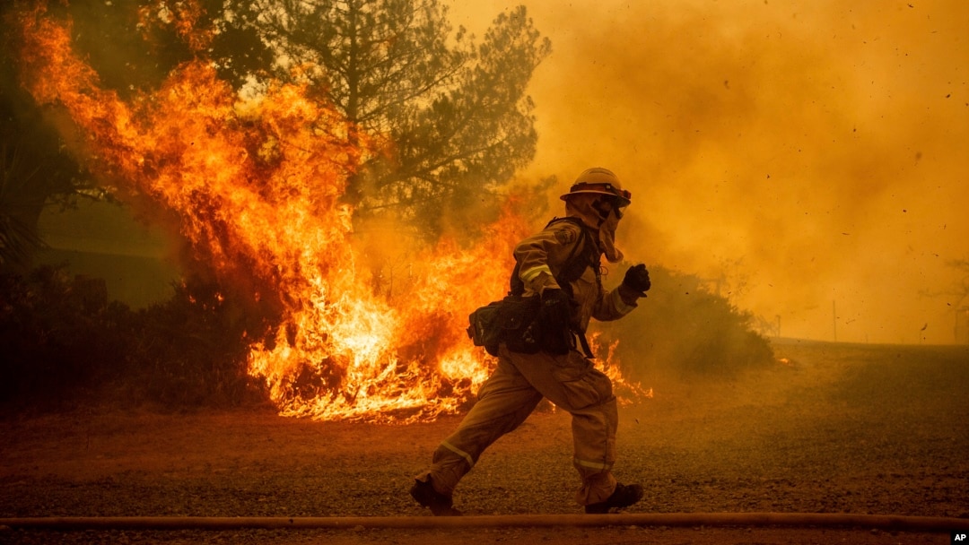 A firefighter runs while trying to save a home as a wildfire tears through Lakeport, Calif., Tuesday, July 31, 2018.