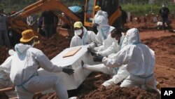 Workers in protective gear lower a coffin of a COVID-19 victim for burial at the special section of the Pedurenan cemetery designated to accommodate the surge in deaths during the coronavirus outbreak in Bekasi, West Java, Indonesia.