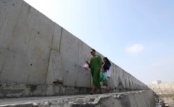 Women walk near a giant sea wall used to prevent sea water from flowing into Jakarta, Indonesia, July 27, 2019. Indonesia's president wants to see the speedy construction of the giant sea wall to save the capital from sinking under the sea.