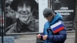 Un hombre lleva una bandera rusa frente a una exposición de fotografías callejeras del Ministerio de Defensa de Rusia que muestra a participantes de eventos en Ucrania, durante la celebración del Día de la Unidad Nacional en Rusia, 2023. [Foto: Archivo/AP]
