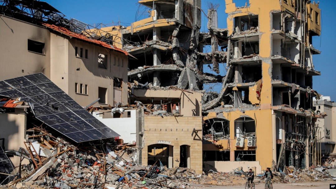 Warga Palestina mengendarai sepeda melewati bangunan yang hancur di Kota Gaza, 29 November 2023, hari keenam gencatan senjata sementara antara Hamas dan Israel. 