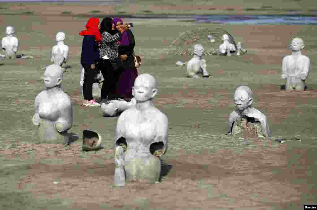 Women take pictures of half-buried stone sculptures at the Lapindo mud field in Sidoarjo. Disaster tourism has become more common in Indonesia, where visitors are drawn to sites of earthquakes, floods and volcanic eruptions to witness the aftermath of catastrophes or simply do some soul-searching.