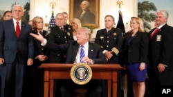 President Donald Trump, with Vice President Mike Pence, left, flanked by members of law enforcement, gestures while speaking before signing a bill in the Diplomatic Reception Room at the White House, June 2, 2017, in Washington. 