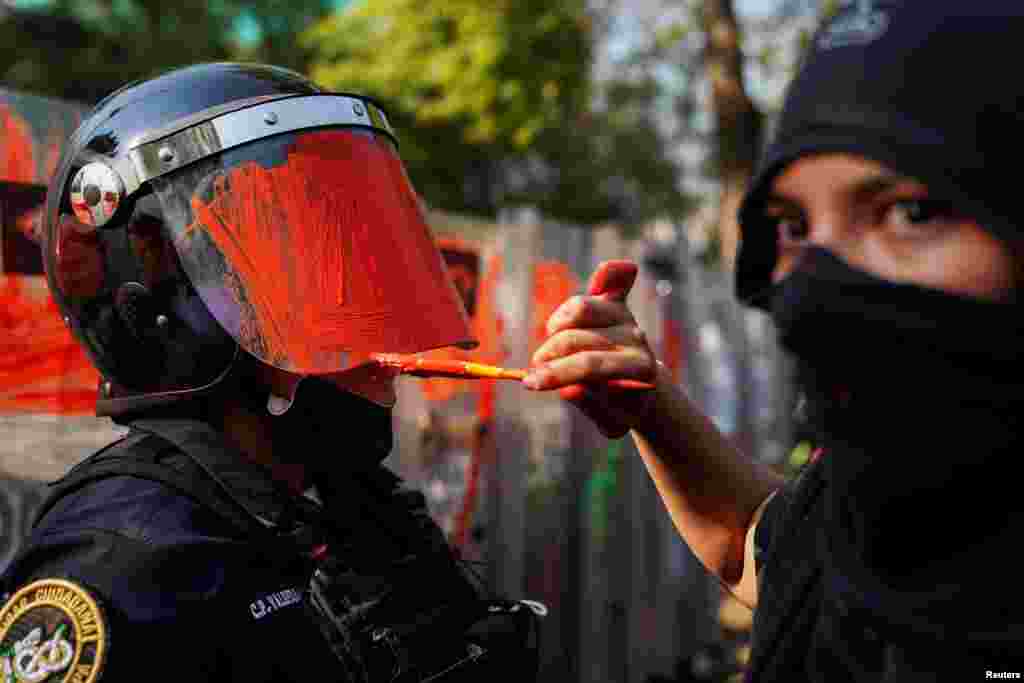 A member of a feminist collective paints the head gear of a riot police officer during a protest against gender and police violence, in Mexico City, Mexico, November 11, 2020.