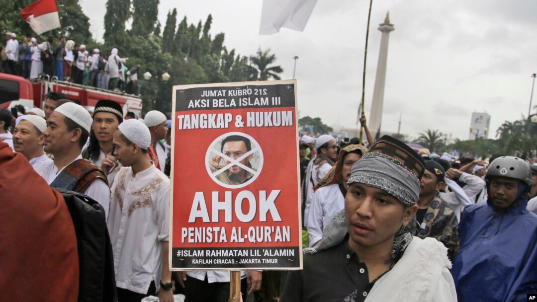 Seorang pendemo memegang poster dalam demonstrasi di Monas, untuk memprotes Gubernur Jakarta Basuki "Ahok" Tjahja Purnama yang pada saat itu menjalani sidang penodaan agama, 2 Desember 2017. 