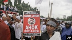 Seorang pendemo memegang poster dalam demonstrasi di Monas, untuk memprotes Gubernur Jakarta Basuki "Ahok" Tjahja Purnama yang pada saat itu menjalani sidang penodaan agama, 2 Desember 2017. 