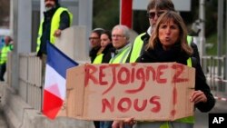 A demonstrator holds a placard reading "Join us" as protesters stand by toll gates on a motorway at Biarritz southwestern France, Dec. 5, 2018. 