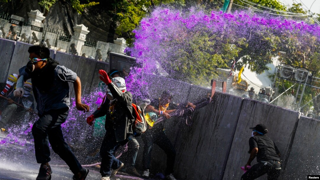 Para demonstran anti-pemerintah melarikan diri seiring penggunaan meriam air oleh polisi anti-huru hara dalam bentrokan dekat markas polisi Bangkok (2/12).