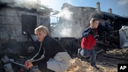 Una mujer frente a su casa quemada mientras su hija juega en un barrio de Donetsk, al este de Ucrania.