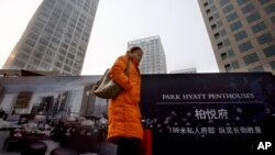 FILE - A Chinese woman walks past a property advertisement on display against residential buildings in Beijing.