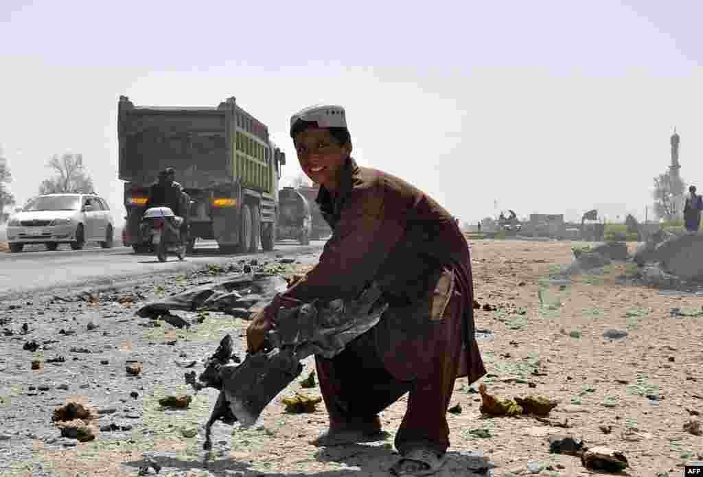 An Afghan child lifts a piece of mangled wreckage from a vehicle at the scene of a blast in Kandahar, Afghanistan.&nbsp;