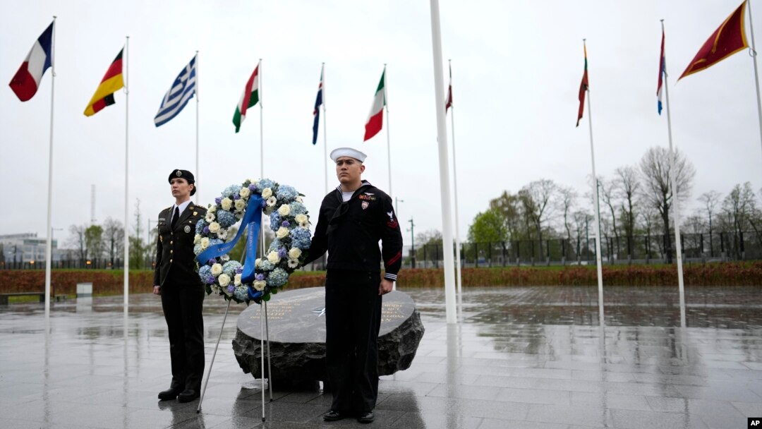 Dos militares se ven bajo las banderas de los estados miembros de la OTAN durante una ofrenda floral en la sede de la alianza en Bruselas, el jueves 4 de abril de 2024. La OTAN celebra el jueves 75 años desde la firma de su tratado fundacional.