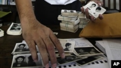 In this photo taken on Aug. 20, 2012, Director of Documentation Center of Cambodia, Youk Chhang arranges photos, a part of about a thousand of newly-discovered photo collection of detainees at the former Khmer Rouge main prison S-21, in his office in Phnom Penh, Cambodia. More than three decades have passed since the Khmer Rouge ultras orchestrated the deaths of nearly 2 million, one out of every four Cambodians, and turned the country into a slave labor camp. (AP Photo/Heng Sinith)