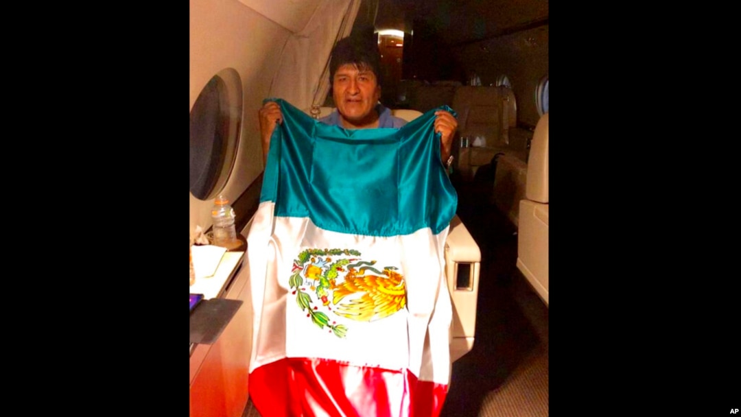 En esta imagen publicada por el ministro mexicano de Exteriores, Marcelo Ebrarde, se ve al expresidente de Bolivia Evo Morales sosteniendo una bandera mexicana a bordo de un avión de la Fuerza Aérea mexicana.