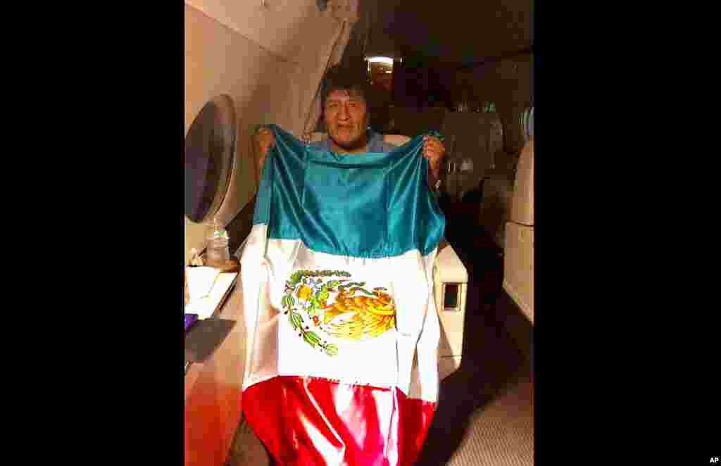 En esta imagen publicada por el ministro mexicano de Exteriores, Marcelo Ebrard, se ve al expresidente de Bolivia Evo Morales sosteniendo una bandera mexicana a bordo de un avión de la Fuerza Aérea mexicana, el lunes 11 de noviembre de 2019.