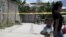 FILE - A woman and a child walk past a crime scene where the body of a dead man was found after he was shot by alleged gang members in the El Castillo neighborhood in Soyapango, on the outskirts of San Salvador, El Salvador, July 20, 2015.