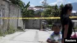 FILE - A woman and a child walk past a crime scene where the body of a dead man was found after he was shot by alleged gang members in the El Castillo neighborhood in Soyapango, on the outskirts of San Salvador, El Salvador, July 20, 2015.