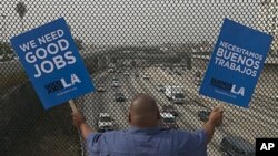 South Los Angeles resident Christian Del Cid waves banners calling for good jobs, on a bridge in front of oncoming traffic at the Interstate I-110 overpass on a "structurally deficient" bridge to call on U.S. Congress to provide funding for highway improv