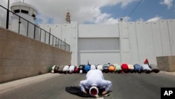 Palestinians perform Friday Prayers in front of a checkpoint along Israel's separation barrier during a demonstration to support prisoners on hunger strike in Israeli jails, West Bank town of Bethlehem, June 6, 2014.