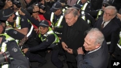 ພະ Cardinal George Pell, ກາງຈາກຂວາ, ຖືກອ້ອມລ້ອມ ໂດຍຕຳຫຼວດ ໃນຂະນະທີ່ເພີ່ນໄປຮອດ ສານຊັ້ນຕົ້ນ ໃນນະຄອນ Melbourne, ອອສເຕຣເລຍ, ວັນທີ 26 ກໍລະກົດ 2017. 