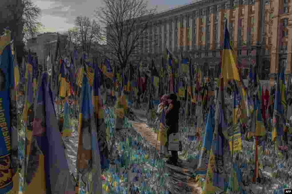 Visitors stand next to a makeshift memorial paying tribute to Ukrainian and foreign fighters with flags at the Independence Square in Kyiv ahead of the third anniversary of Russia&#39;s invasion of Ukraine.