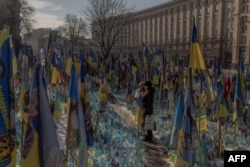 Los visitantes se encuentran junto a un monumento improvisado que rinde homenaje a los combatientes ucranianos y extranjeros con banderas en la Plaza de la Independencia en Kiev, el 23 de febrero de 2025, antes del tercer aniversario de la invasión rusa de Ucrania.