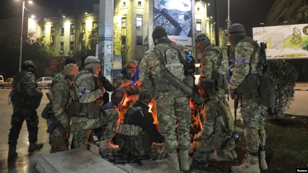 Los combatientes de la oposición siria se reúnen alrededor de una fogata para calentarse en la plaza Saadallah al-Jabiri, después de que los rebeldes opuestos al presidente Bashar al-Assad dijeran que habían llegado al corazón de Alepo.