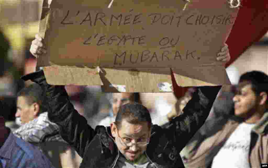 An anti-government protester holds a banner in French referring to the Egyptian President and reading "The army must choose Egypt or Mubarak", at the continuing demonstration in Tahrir square in downtown Cairo, Egypt, Monday, Jan. 31, 2011. A coalition of