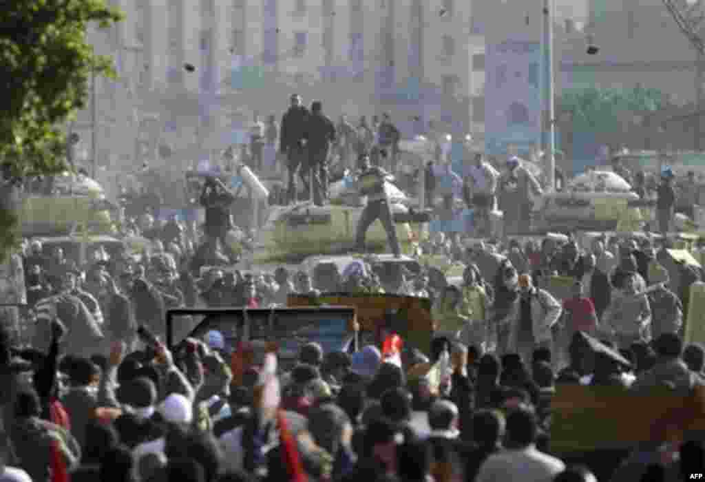 Stones fly through the air as supporters of President Hosni Mubarak, foreground , fight with anti-Mubarak protesters, rear, standing on army tanks in Cairo, Egypt, Wednesday, Feb.2, 2011. Several thousand supporters of Mubarak, including some riding hors