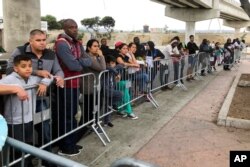 FILE - Asylum seekers in Tijuana, Mexico, listen to names being called from a waiting list to allow them an opportunity to make their case, at a border crossing in San Diego, California, Sept. 26, 2019.