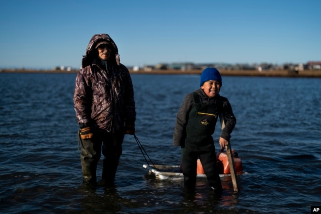 Joe Eningowuk, 62, and his grandson, Isaiah Kakoona, 7, stand for a photo in the lagoon while getting ready for a camping trip in Shishmaref, Alaska, Saturday, Oct. 1, 2022. (AP Photo/Jae C. Hong)