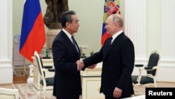 Presiden Rusia Vladimir Putin berjabat tangan dengan Wang Yi saat ia masih menjabat sebagai Direktur Kantor Komisi Luar Negeri Pusat China, Moskow, Rusia 22 Februari 2023. (Foto: Sputnik/Anton Novoderezhkin/Pool via REUTERS)