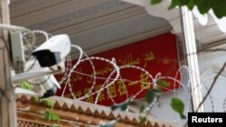 FILE - A propaganda banner and a security camera are placed on the walls of a mosque in the Old City in Kashgar, Xinjiang Uighur Autonomous Region, China, Sept. 6, 2018. 