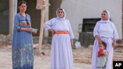 Yazidi women in traditional clothing stand outside their houses in the village of Dugure in Sinjar, Iraq, July 16, 2024.