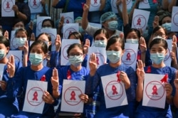 Maestros de la Universidad de Educación de Rangún muestras cintas rojas y hacen el saludo de tres dedos durante una manifestación en Rangún, Birmania, el 5 de febrero de 2021, contra el golpe militar de inicios de la semana.