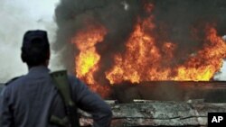 Pakistani police officer stands guard on still smoldering oil trucks in Shikarpur, southern Pakistan, 01 Oct. 2010