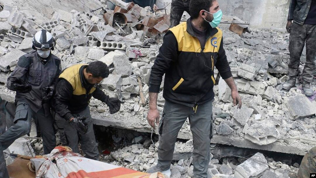 This photo released March 13, 2018, by the Syrian Civil Defense group known as the White Helmets, shows members of the White Hemets removing a body after airstrikes and shelling by Syrian government forces, in Ghouta. 
