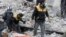 This photo released March 13, 2018, by the Syrian Civil Defense group known as the White Helmets, shows members of the White Hemets removing a body after airstrikes and shelling by Syrian government forces, in Ghouta. 