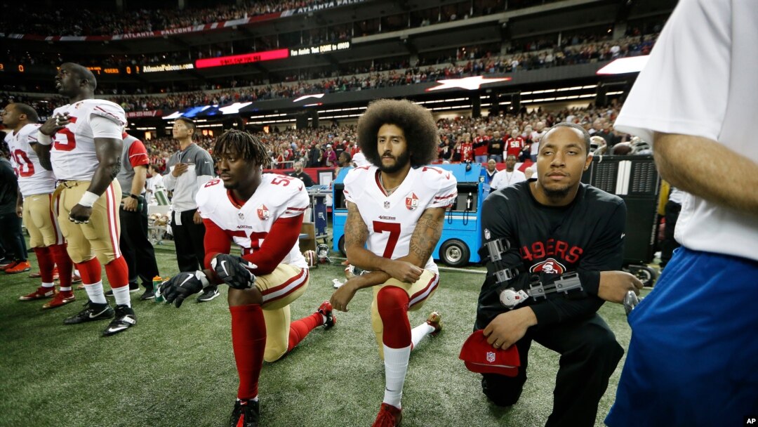 Colin Kaepernick, en el centro, arrodillándose al sonar el himno nacional al comienzo de un encuentro, un gesto que se convirtió en un símbolo y que le costó su carrera como jugador de fútbol americano.