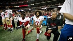 Colin Kaepernick, en el centro, arrodillándose al sonar el himno nacional al comienzo de un encuentro, un gesto que se convirtió en un símbolo y que le costó su carrera como jugador de fútbol americano.