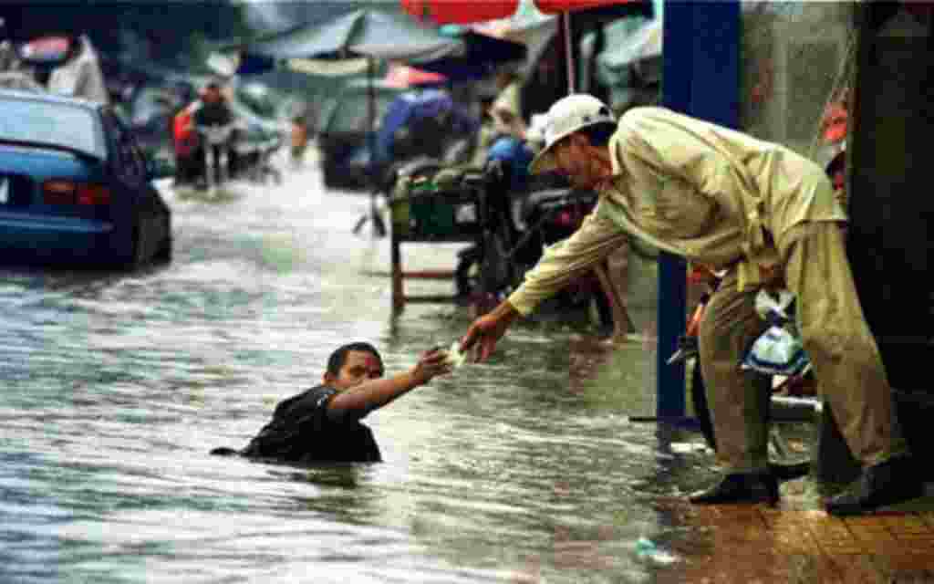 A Cambodian amputee beggar is given money by a passerby while wading in the street flood in Phnom Penh.