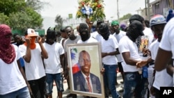 Para anggota geng G9 yang dipimpin oleh Jimmy Cherizier alias Barbecue, memegang foto Presiden Jovenel Moise yang tewas terbunuh. Kelompok G9 melakukan unjuk rasa menuntut keadilan atas pembunuhan tersebut di Port-au-Prince pada 26 Juli 2021. (Foto: AP/Matias Delacroix)