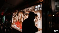 在北京街头一个公交车站一名男子走过显示中国志愿军参加朝鲜战争的电影“金刚川”的广告箱。（2020年10月22日）