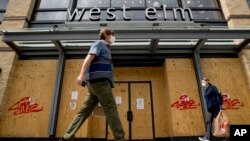 People in masks walk past a boarded up storefront in Washington, D.C., April 29, 2020. 