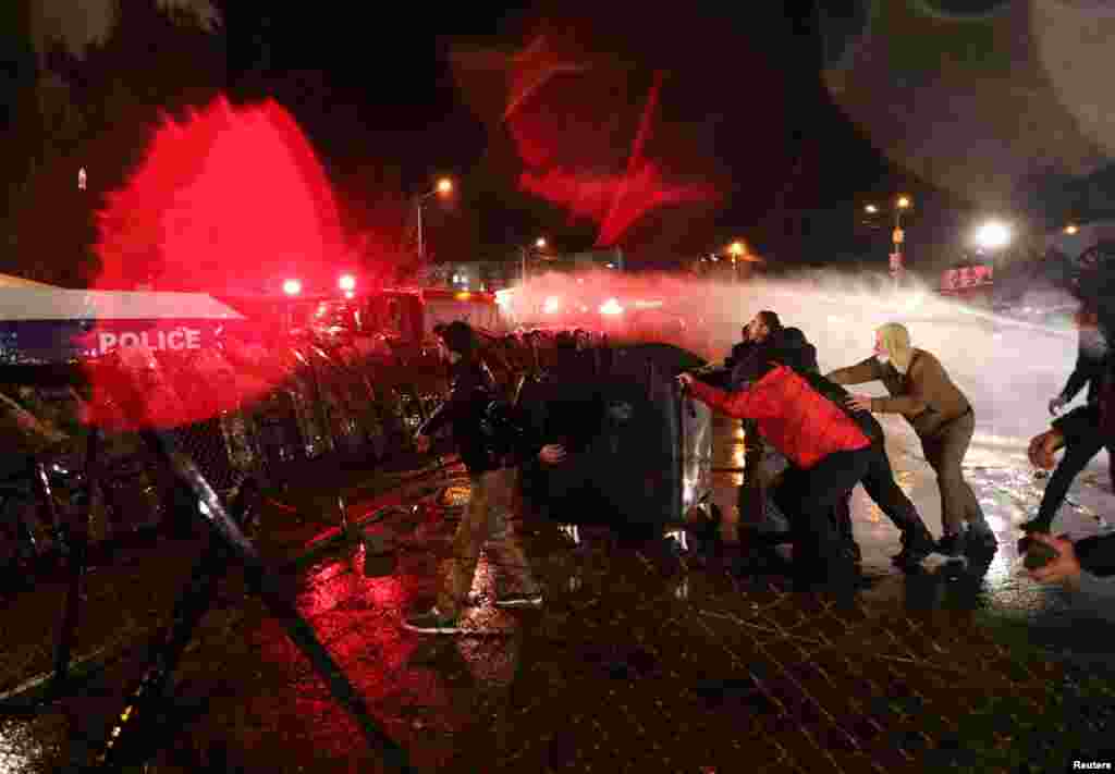 Demonstrators react as riot police use a water cannon during an opposition rally against the results of a parliamentary election, outside the Central Election Commission (CEC) building in Tbilisi, Georgia, Nov. 8, 2020.