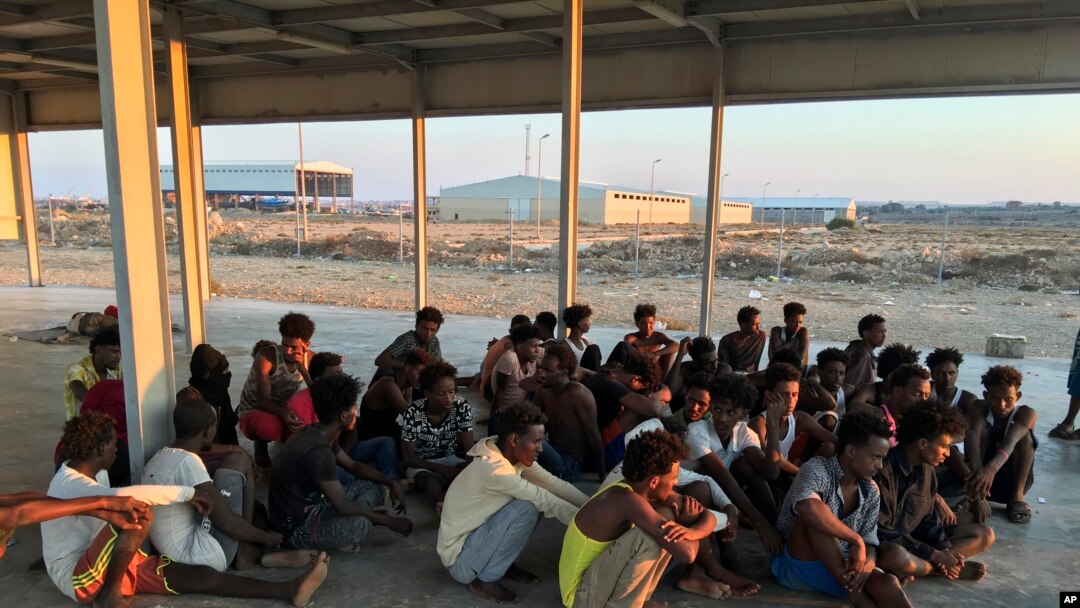 Rescued migrants sit on a coast about 100 kilometers (60 miles) east of Tripoli, Libya, July 25, 2019. The U.N. refugee agency and the International Rescue Committee say up to 150 may have perished at sea off the coast of Libya.