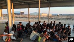 Rescued migrants sit on a coast about 100 kilometers (60 miles) east of Tripoli, Libya, July 25, 2019. The U.N. refugee agency and the International Rescue Committee say up to 150 may have perished at sea off the coast of Libya.