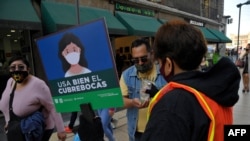 Un trabajador de la secretaría de Turismo con un cartel que dice “Usar correctamente la mascarilla” ofrece gel antibacteriano a los peatones en el centro histórico de Ciudad de México, el 19 de noviembre de 2020.